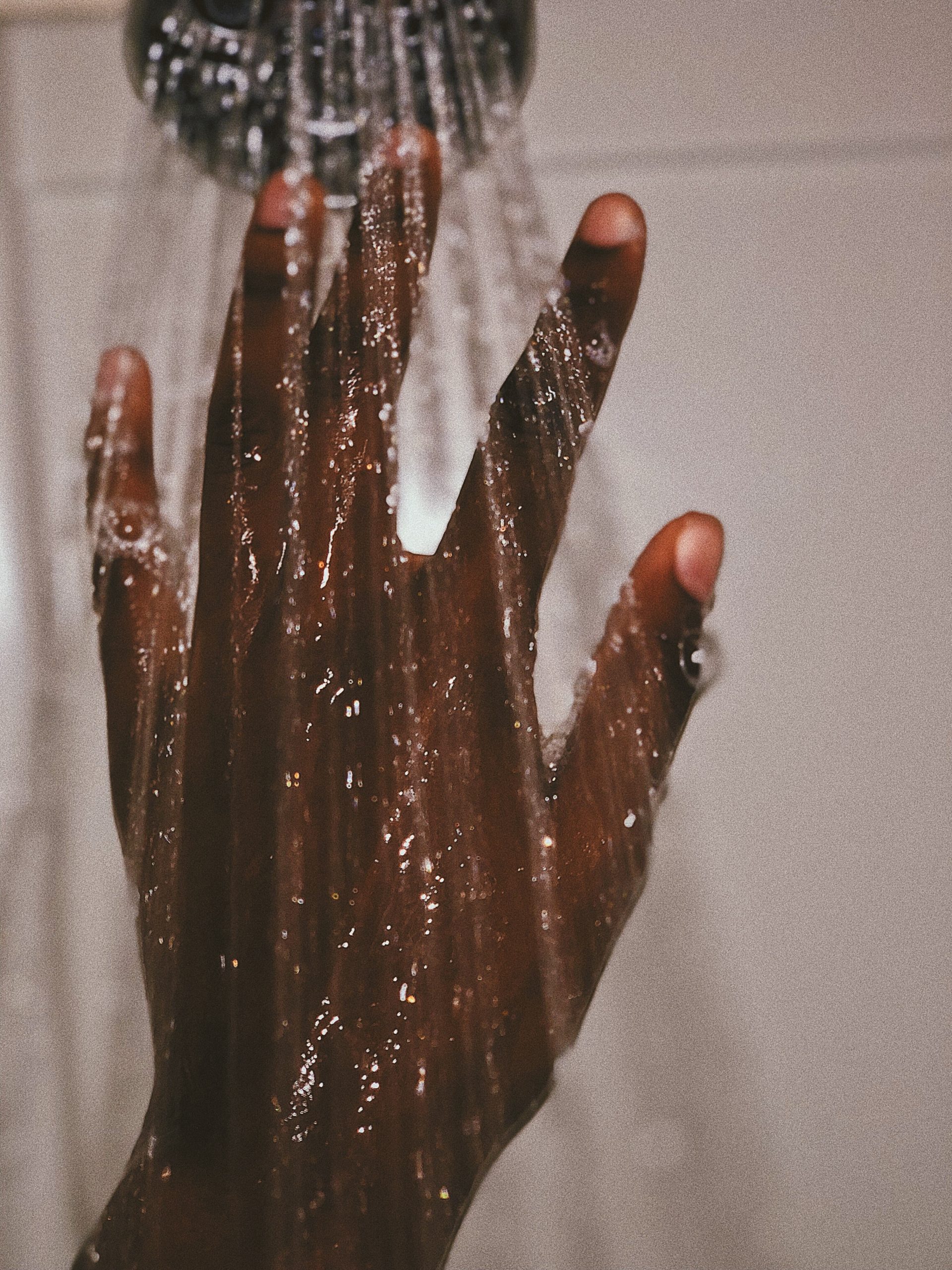 Schwarze Hand greift in den Wasserstrahl einer Dusche. Für viele Menschen ist der Zugang zu sauberem Wasser nicht selbstverständlich.